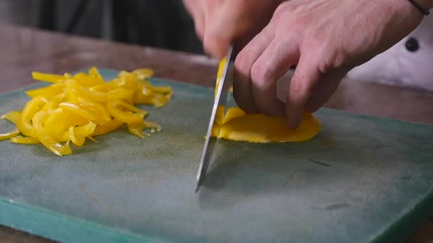 Повільний рух шеф-кухаря, який ріже жовтий перець з овочами на задньому плані — стокове відео