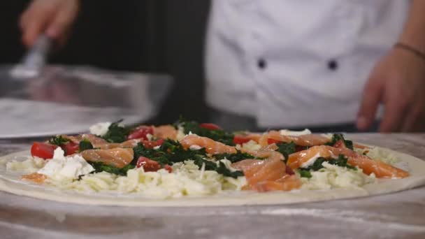 Отслеживание крупным планом размещения невыпеченной пиццы с начинками из мучного стола на металлической кожуре — стоковое видео