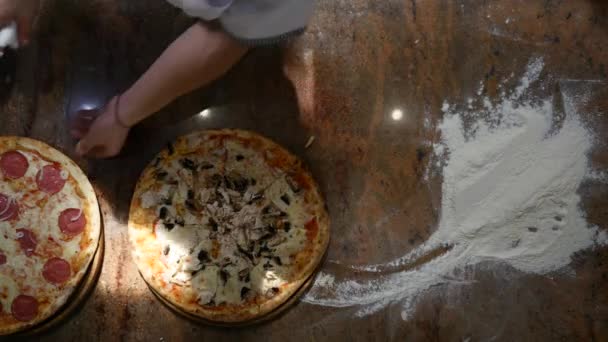 Hiermee snijdt u de pizza op een donkere achtergrond in de keuken — Stockvideo