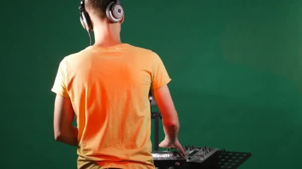 El DJ mezclando música de pie en su cubierta, bailando en su auricular, desde la parte posterior — Vídeo de stock