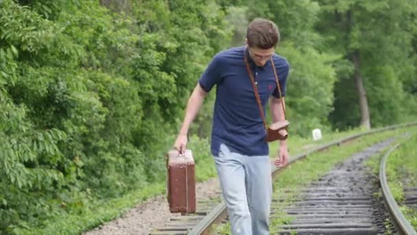 年轻的男人带着手提箱在铁路线上。火车在一个大的城市，失去一名年轻男子去迷失在大城市 — 图库视频影像