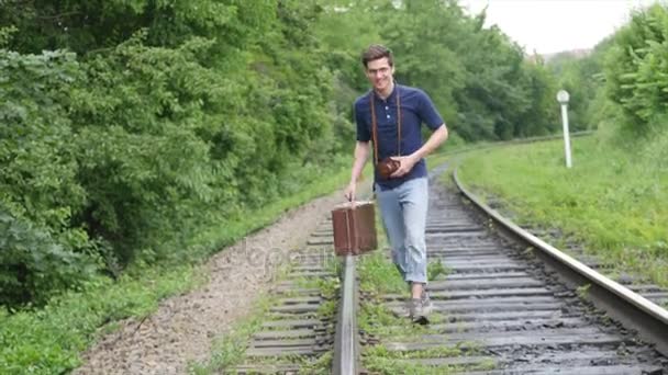 Un giovanotto con una valigia sulla linea ferroviaria. Il treno perde in una grande città, un giovane va a perdersi nella grande città — Video Stock