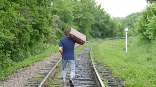 Un joven con una maleta en la línea ferroviaria. Tren pierde en una gran ciudad, un joven va a perderse en la gran ciudad — Vídeos de Stock