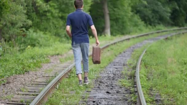 Un joven con una maleta en la línea ferroviaria. Tren pierde en una gran ciudad, un joven va a perderse en la gran ciudad — Vídeos de Stock