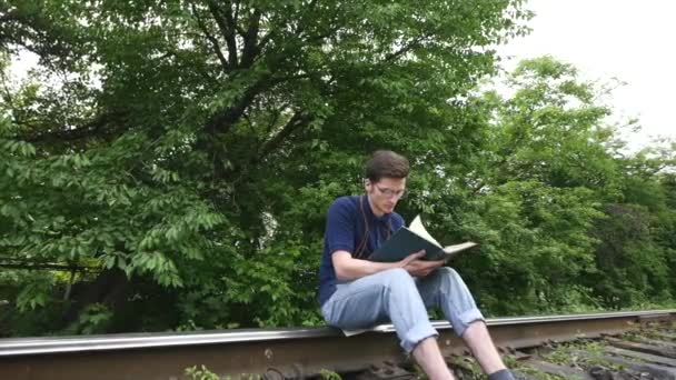 Молодий чоловік читає книгу на залізничній колії — стокове відео