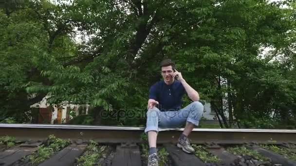 Young man speaks by phone on a railway track — Stock Video