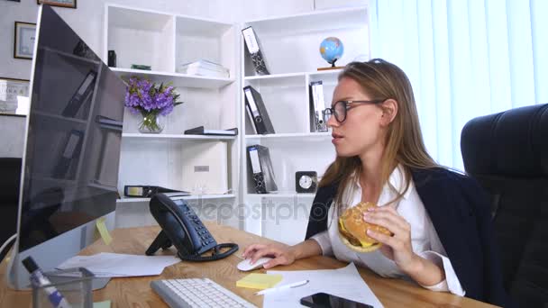 Занятая женщина разговаривает по телефону, когда ест бургер — стоковое видео