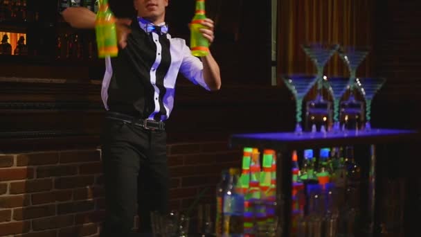 Acrobatische show uitgevoerd door barman jongleren twee flessen. Bar achtergrond. Slow-motion. selectieve aandacht — Stockvideo