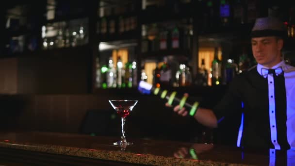 Giovane, attraente barista professionista, barista fare fresco, professionale, trucchi incredibili con due bottiglie, cattura sul gomito, vomitare, in piedi dietro il bar, spettacolo di fuoco. rallentatore — Video Stock