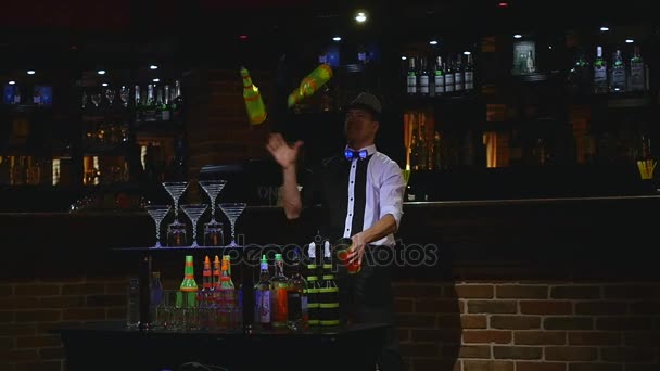 Акробатическое шоу в исполнении бармена, жонглирующего двумя бутылками и Бикером для микширования. фон бара. замедленное движение — стоковое видео