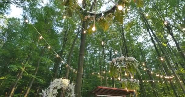Gloeilampen buiten over een draad tegen zonsondergang bos, concept vakantie, lampen en gloed hangen de boom in het bos, oranje, lamp decoratie tuin 's nachts, glas lantaarn — Stockvideo