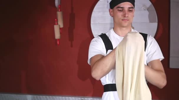 Young man spinning and throwing dough up in the air with two hands in kitchen of restaurant — Stock Video