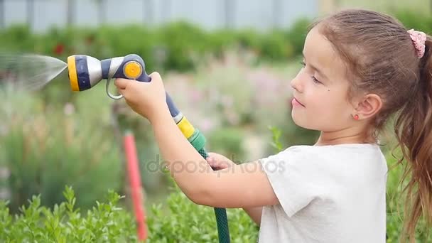 Linda niña sosteniendo una manguera de agua y agitándola mientras riega el césped — Vídeo de stock