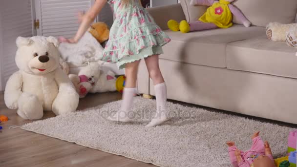 Menina loira feliz no vestido se divertindo dançando dentro de casa em uma sala branca ensolarada em casa ou jardim de infância — Vídeo de Stock