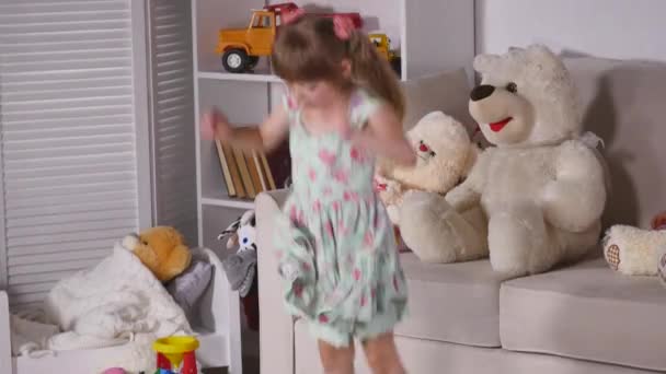 Ευτυχισμένος ξανθό κορίτσι στο φόρεμα διασκεδάζουν χορεύοντας σε εσωτερικούς χώρους σε ένα ηλιόλουστο δωμάτιο στο σπίτι με το λευκό ή το νηπιαγωγείο — Αρχείο Βίντεο