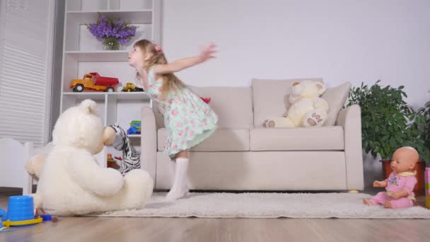 Bonne fille blonde dans la robe s'amuser à danser à l'intérieur dans une chambre blanche ensoleillée à la maison ou à la maternelle — Video