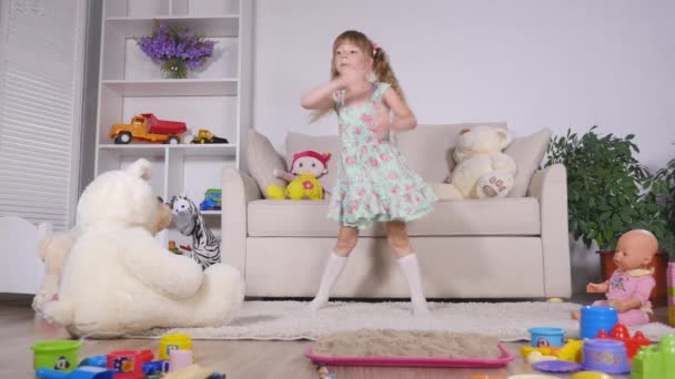 Gelukkig blond meisje in de jurk plezier dansen binnenshuis in een zonnige witte kamer thuis of kleuterschool — Stockvideo