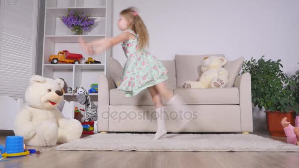 Bonne fille blonde dans la robe s'amuser à danser à l'intérieur dans une chambre blanche ensoleillée à la maison ou à la maternelle — Video