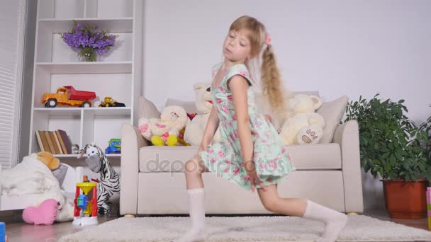 Chica rubia feliz en el vestido que se divierte bailando en el interior en una habitación blanca soleada en casa o jardín de infantes — Vídeos de Stock