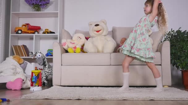 Bonne fille blonde dans la robe s'amuser à danser à l'intérieur dans une chambre blanche ensoleillée à la maison ou à la maternelle — Video