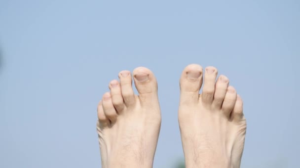 Los pies de hombre en el fondo del cielo. Una persona feliz relajándose y tomando un baño de sol — Vídeos de Stock