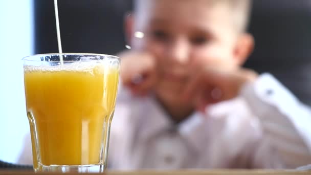 Gieten in glas sinaasappelsap. kleine jongen achtergrond. selectieve aandacht — Stockvideo