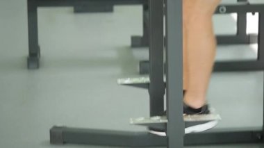 Genç sakallı biri bir spor salonunda yatay bir çubuk üzerinde kaldırma bacak yapıyor çıplak bir gövde ile aşağı eğimli