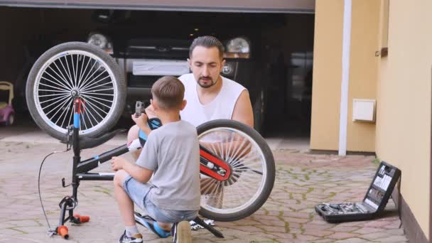 Apa és fia rögzítése egy kerékpár, egy napsütéses napon — Stock videók