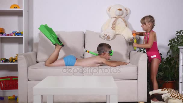 Two happy kids in swimsuits. Boy in diving mask Float on the couch and The girl is blowing bubbles in room — Stock Video