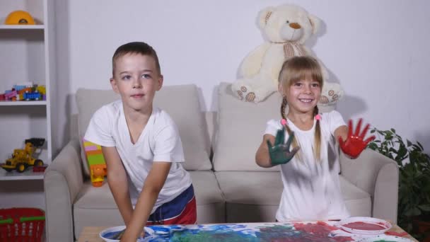 Un niño divertido lindo feliz pintando huellas de manos de color en la hoja blanca de papel — Vídeo de stock