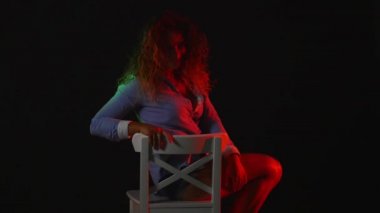 Seksi bir kız bir inç kısa şort ve tişört siyah arka plan üzerine bir sandalyede oturur