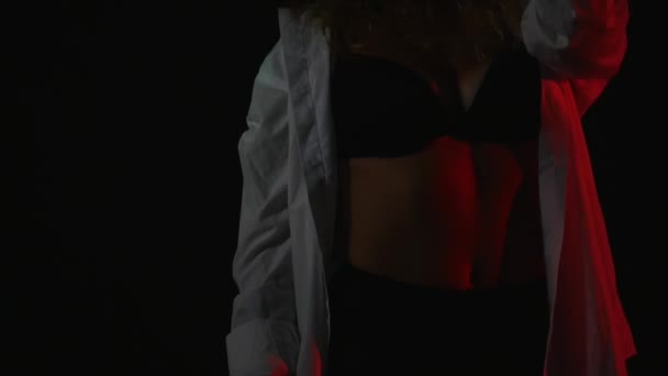 Εσωτερικη ευτυχισμένη νεαρή γυναίκα με κόκκινα μαλλιά φορώντας ξεκούμπωτο πουκάμισο και σέξι σουτιέν μαύρο σε μαύρο φόντο — Αρχείο Βίντεο