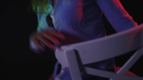 Egy szexi lány ül egy széken, egy a rövid nadrág és egy póló, fekete háttér — Stock videók
