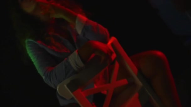 Sexy dívka sedí na židli v krátké šortky a tričko na černém pozadí — Stock video