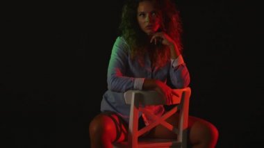 Seksi bir kız bir inç kısa şort ve tişört siyah arka plan üzerine bir sandalyede oturur