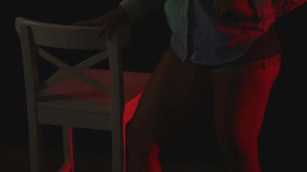 Sexy czerwone kobiet w krótkie spodenki i koszulkę, taniec w ciemności w pobliżu krzesło — Wideo stockowe