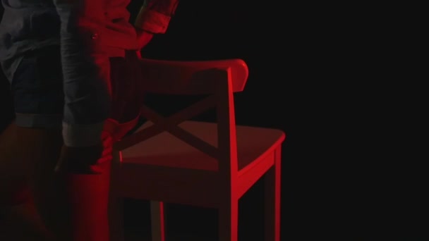 Sexig röd kvinnor i korta shorts och en tröja som dansar i mörkret nära stol — Stockvideo