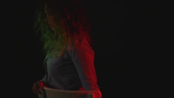 一个性感的女孩坐在椅子上的短的短裤和一件衬衫在黑色背景上 — 图库视频影像