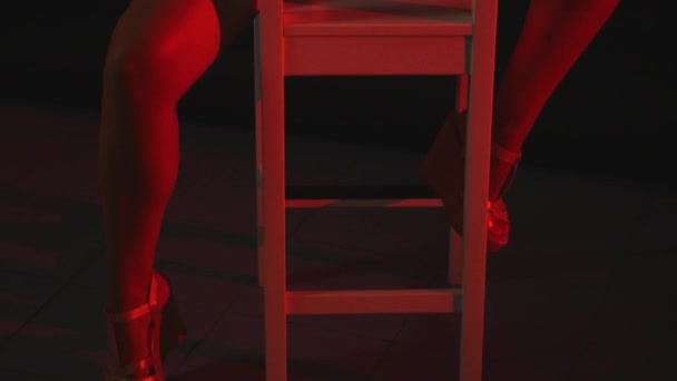 Una chica sexy se sienta en una silla en pantalones cortos y una camisa sobre fondo negro — Vídeo de stock