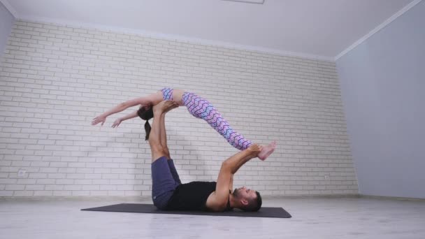 Mooie paar acro yoga beoefenen. Jonge yoga-instructeurs praktijk in een studio. Twee succesvolle jonge mensen voeren acro yoga oefeningen — Stockvideo