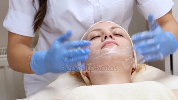 Femme est allongée sur le canapé pendant la procédure cosmétique. Cosmétologue professionnel fait le massage du visage dans le salon de spa. Soins du visage. Concept beauté, santé et jeunesse — Video