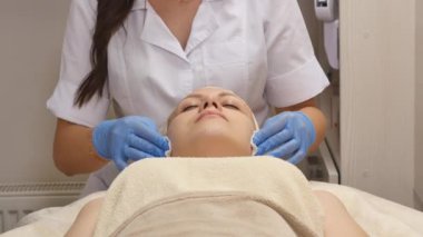 Güzel bir kadın kozmetik masanın üzerinde profesyonel olarak hastanın yüz temizlemek için pamuk sünger kullanarak dermatolog yatan Kapalı gözlerle. Yüz bakımı, sağlıklı olmak mutlu olmak,