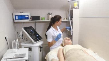 Genç güzel kadın klinik tabloyu, güzellik uzmanı yalan onu yüz elektro-stimülasyon masaj yapar. Kaldırma yordamı, donanım kozmetik. Lüks yaşam tarzı, modeli faaliyetleri