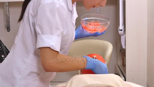 Mujer joven recibiendo un tratamiento de spa medicina cosmética hecho, de cerca. Las manos esteticistas en el trabajo, la aplicación de la máscara facial de arcilla en una hermosa cara de niña, hidratando la piel — Vídeos de Stock