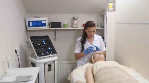 Una mujer bonita con los ojos cerrados, acostado en la mesa de los cosmetólogos, el dermatólogo profesionalmente limpiar la cara de la paciente. Cuidado facial, ser feliz, estar sano — Vídeo de stock