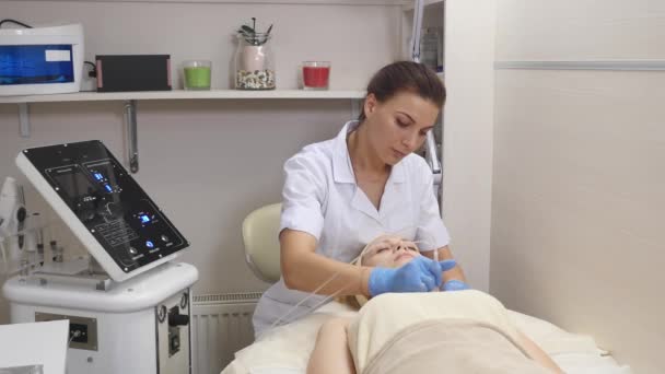 Joven hermosa mujer acostada en la mesa clínica, el cosmetólogo le hace un masaje de electro-estimulación facial. Procedimiento de elevación, cosmetología de hardware. Estilo de vida de lujo, actividades modelo — Vídeos de Stock