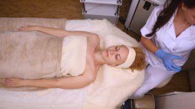 Güzel bir kadın kozmetik masanın üzerinde profesyonel olarak hastanın yüz temizlemek için pamuk sünger kullanarak dermatolog yatan Kapalı gözlerle. Yüz bakımı, sağlıklı olmak mutlu olmak. Sayfanın Üstü