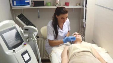 Güzel bir kadın kozmetik masanın üzerinde profesyonel olarak hastanın yüz temizlemek için pamuk sünger kullanarak dermatolog yatan Kapalı gözlerle. Yüz bakımı, sağlıklı olmak mutlu olmak,