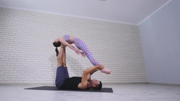 Hermosa pareja practicando acro yoga. Jóvenes instructores de yoga practican en un estudio. Dos jóvenes exitosos realizan ejercicios de acro yoga — Vídeos de Stock