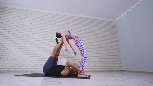 Belo casal praticando acro ioga. Jovens instrutores de ioga praticam em um estúdio. Dois jovens bem sucedidos realizam exercícios de acro ioga — Fotografia de Stock